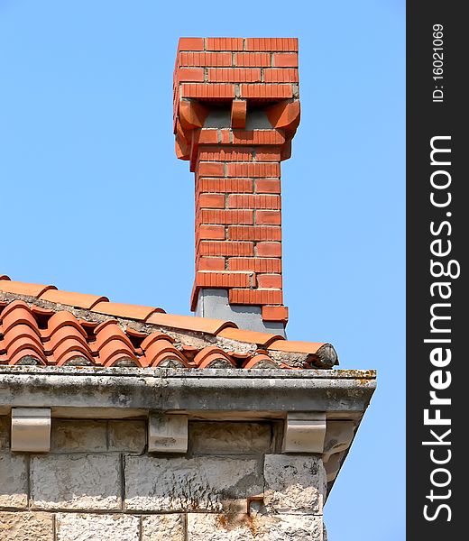 Closeup of the old tiled roof and new red chimney on the blue sky.