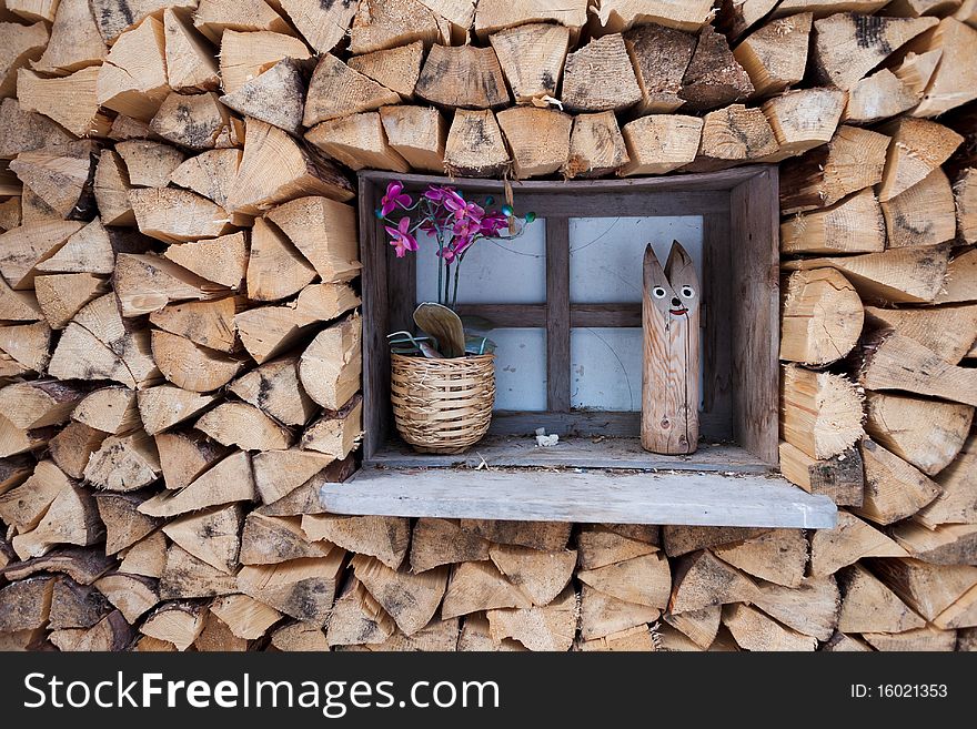 Wooden window with orchid in a pot and wooden cat among stock of wooden logs. Wooden window with orchid in a pot and wooden cat among stock of wooden logs.