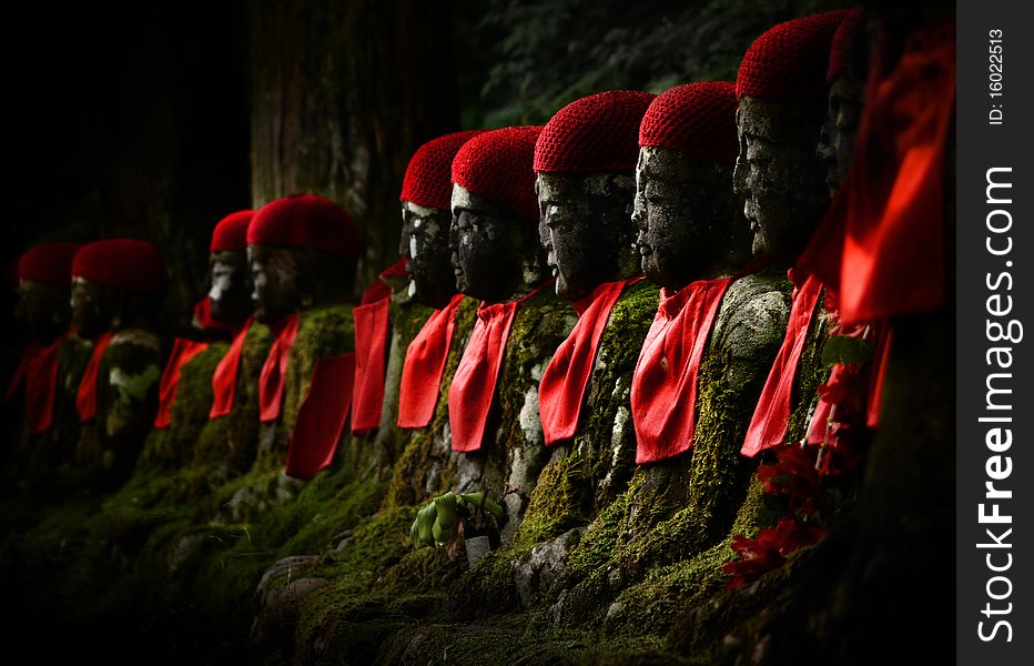 Stone budhhas with red hat side by side in the forest. Stone budhhas with red hat side by side in the forest.