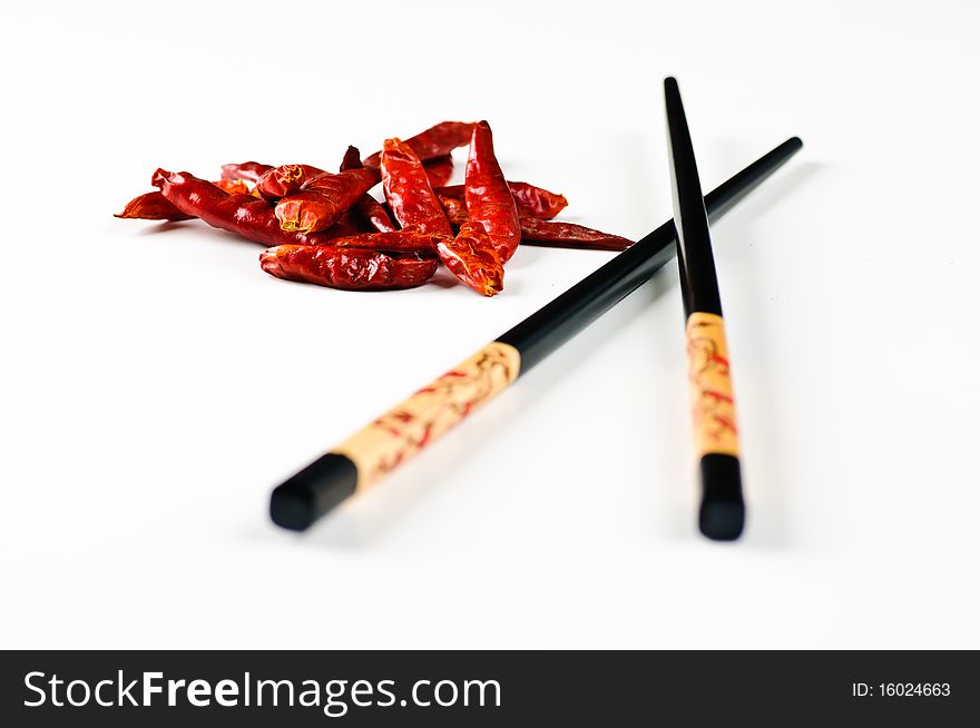 Two chop sticks and some chili fruits on a white background