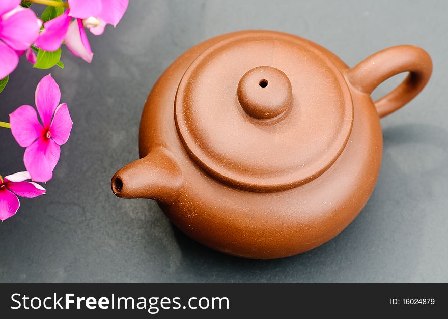 A brown clay tea pot on a table outside next to some flowers