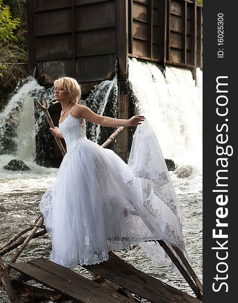 Young blonde woman in a white wedding dress near the waterfall. Young blonde woman in a white wedding dress near the waterfall