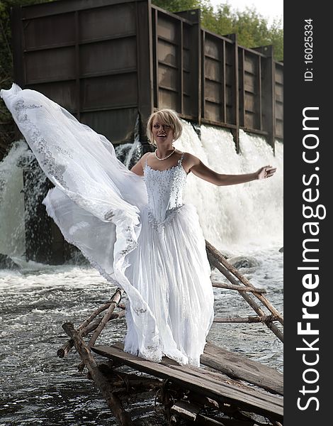 Young blonde woman in a white wedding dress near the waterfall. Young blonde woman in a white wedding dress near the waterfall