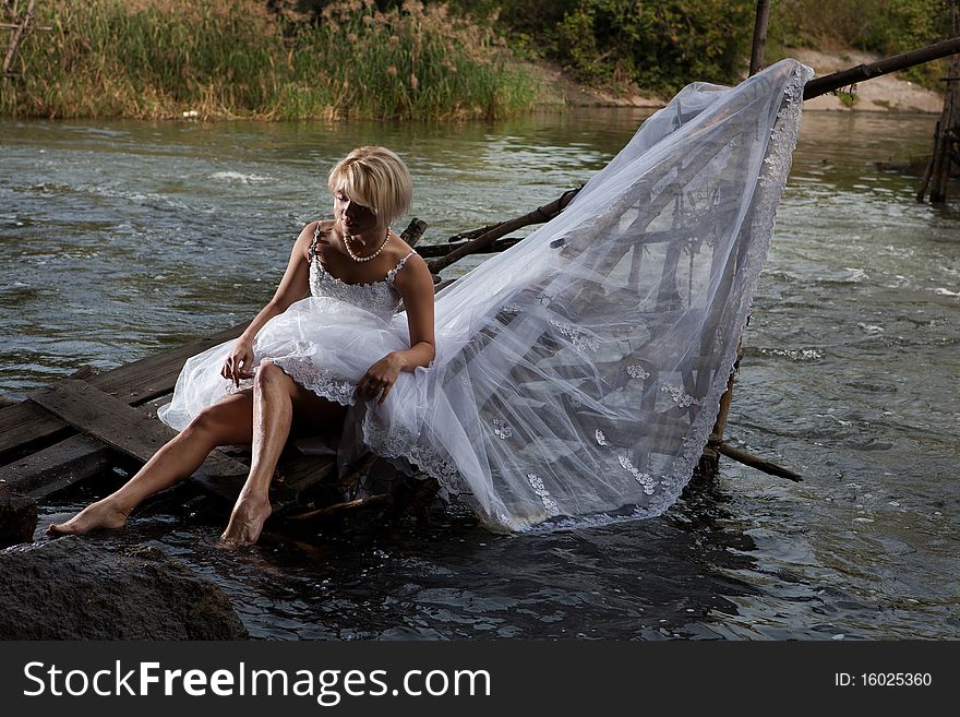 Young blonde woman in a white wedding dress near the waterfall. Young blonde woman in a white wedding dress near the waterfall