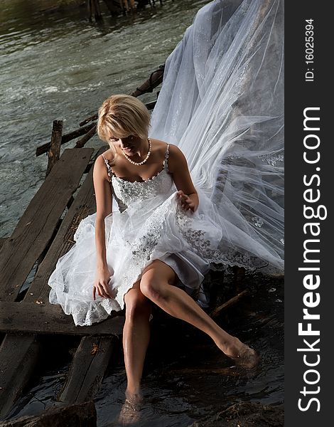 Young blonde woman in a white wedding dress near the waterfall. Young blonde woman in a white wedding dress near the waterfall