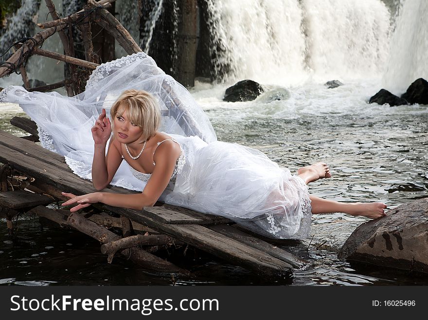 Young blonde woman in a white wedding dress near the waterfall. Young blonde woman in a white wedding dress near the waterfall