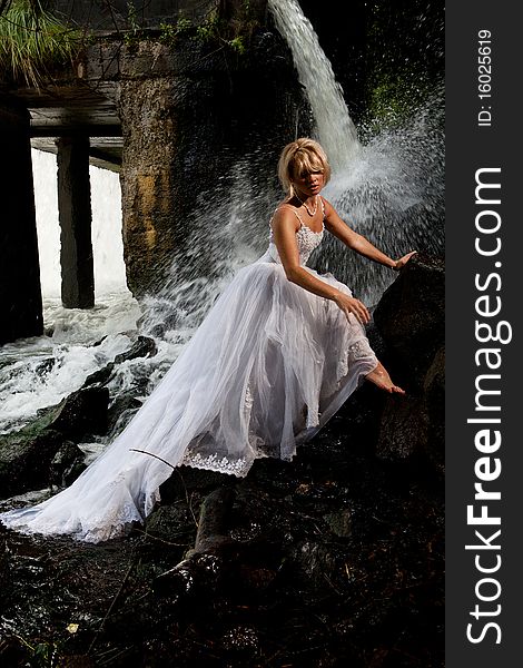 Young blonde woman in a white wedding dress near the waterfall. Young blonde woman in a white wedding dress near the waterfall