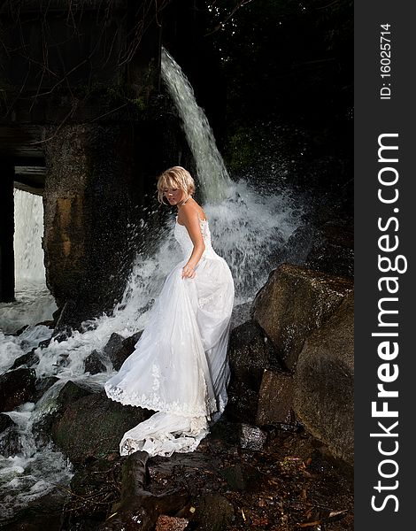 Young blonde woman in a white wedding dress near the waterfall. Young blonde woman in a white wedding dress near the waterfall