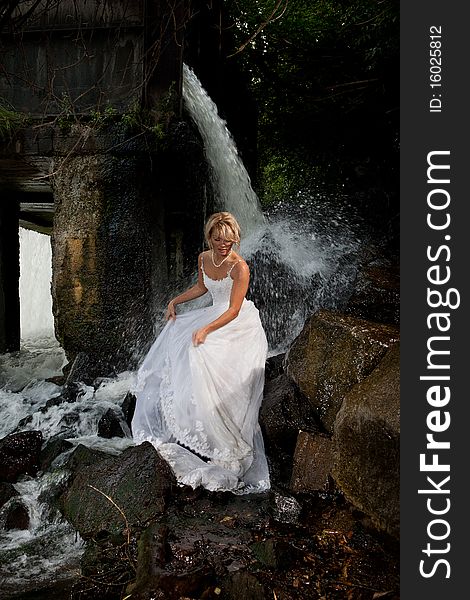 Young blonde woman in a white wedding dress near the waterfall. Young blonde woman in a white wedding dress near the waterfall