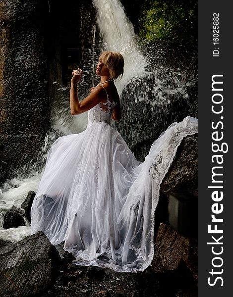 Young blonde woman in a white wedding dress near the waterfall. Young blonde woman in a white wedding dress near the waterfall