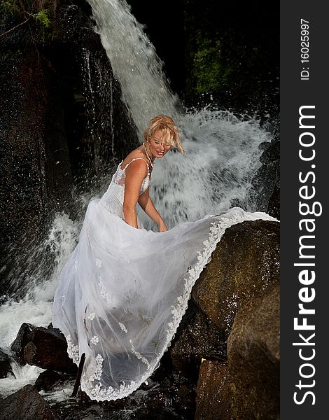 Young blonde woman in a white wedding dress near the waterfall. Young blonde woman in a white wedding dress near the waterfall