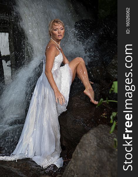 Young blonde woman in a white wedding dress near the waterfall. Young blonde woman in a white wedding dress near the waterfall