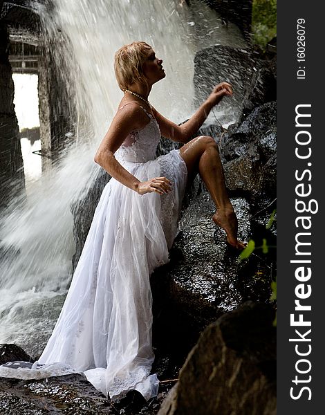 Young blonde woman in a white wedding dress near the waterfall. Young blonde woman in a white wedding dress near the waterfall