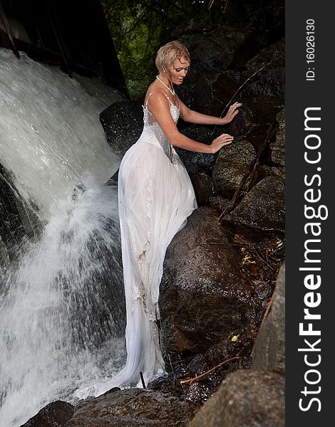Young blonde woman in a white wedding dress near the waterfall. Young blonde woman in a white wedding dress near the waterfall