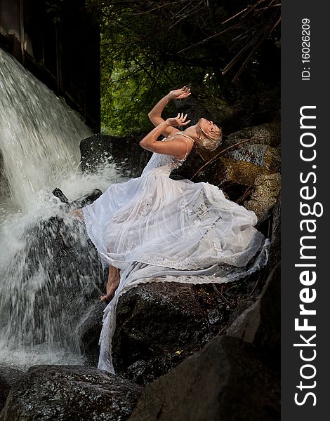 Young blonde woman in a white wedding dress near the waterfall. Young blonde woman in a white wedding dress near the waterfall