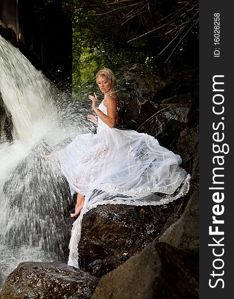 Young blonde woman in a white wedding dress near the waterfall. Young blonde woman in a white wedding dress near the waterfall