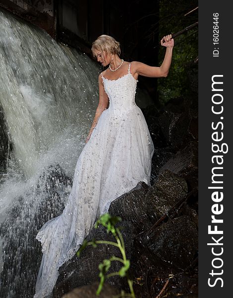 Young blonde woman in a white wedding dress near the waterfall. Young blonde woman in a white wedding dress near the waterfall