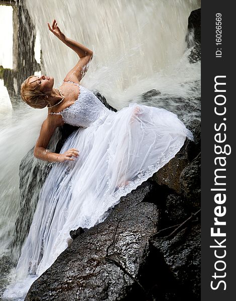 Young blonde woman in a white wedding dress near the waterfall. Young blonde woman in a white wedding dress near the waterfall