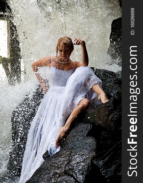 Young blonde woman in a white wedding dress near the waterfall. Young blonde woman in a white wedding dress near the waterfall