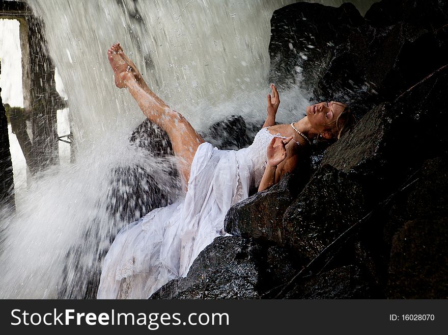 Young blonde woman in a white wedding dress near the waterfall. Young blonde woman in a white wedding dress near the waterfall