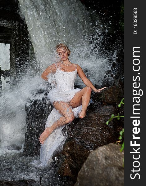 Young blonde woman in a white wedding dress near the waterfall. Young blonde woman in a white wedding dress near the waterfall