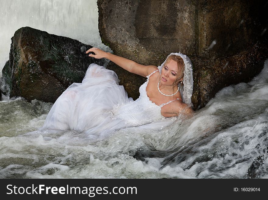 Young blonde woman in a white wedding dress near the waterfall. Young blonde woman in a white wedding dress near the waterfall