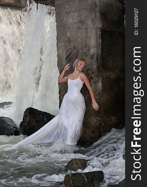 Young blonde woman in a white wedding dress near the waterfall. Young blonde woman in a white wedding dress near the waterfall