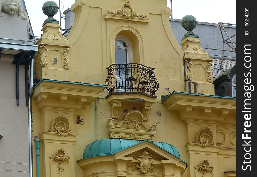 Yellow stucco exterior detail in Baroque stile in downtown Zagreb, Croatia with rich decoration and black wrought iron balcony railing. aged green copper roofing over bay window. tourism concept. Yellow stucco exterior detail in Baroque stile in downtown Zagreb, Croatia with rich decoration and black wrought iron balcony railing. aged green copper roofing over bay window. tourism concept.