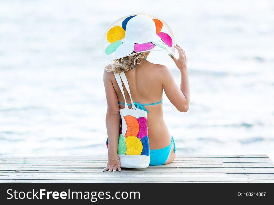 A woman in a hat and bikini is sitting on a wooden pier. A woman in a hat and bikini is sitting on a wooden pier