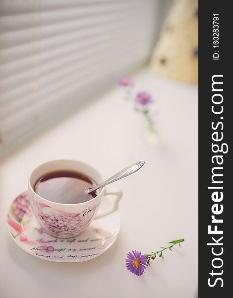 Black tea in an elegant vintage porcelain cup and spoon on the white windowsill.