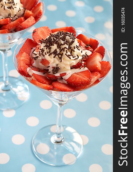 Sliced fresh strawberries with cream and chocolate decoration in martini glasses on blue polka dot background. Sliced fresh strawberries with cream and chocolate decoration in martini glasses on blue polka dot background