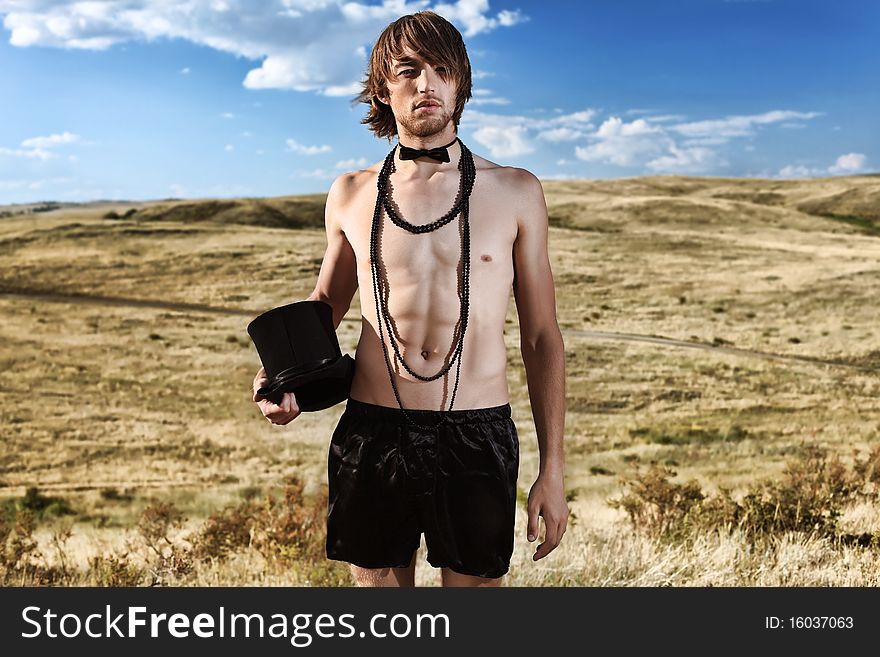 Fashion shot of a handsome young man posing topless in top hat and bow tie over beautiful landscape. Fashion shot of a handsome young man posing topless in top hat and bow tie over beautiful landscape.