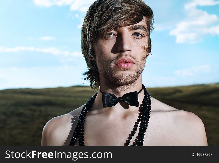 Fashion shot of a handsome young man posing topless in top hat and bow tie over beautiful landscape. Fashion shot of a handsome young man posing topless in top hat and bow tie over beautiful landscape.