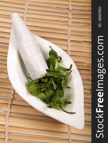White marble mortar and pestle with mint leaves on wooden background.