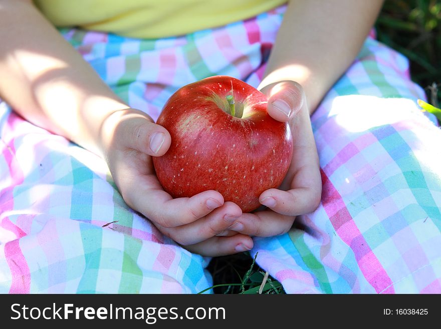 Little girl sitting on a grass and holding red delicious apple. Little girl sitting on a grass and holding red delicious apple