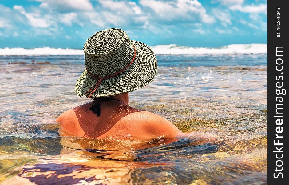 Girl in a green knitted hat floats in the ocean on sunset