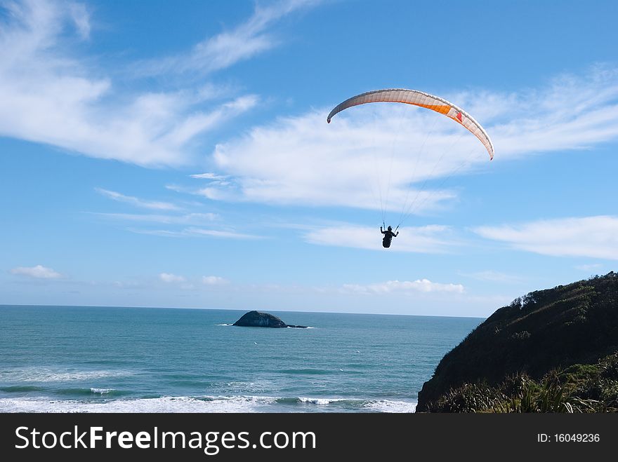 Parachutist in the blue sky flying over the Ocean beach.Mariway beach New Zealand. Parachutist in the blue sky flying over the Ocean beach.Mariway beach New Zealand