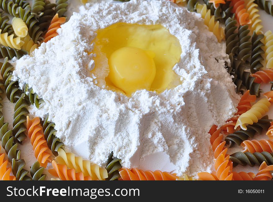 An egg lies in a flour alongside the coloured macaronis. An egg lies in a flour alongside the coloured macaronis