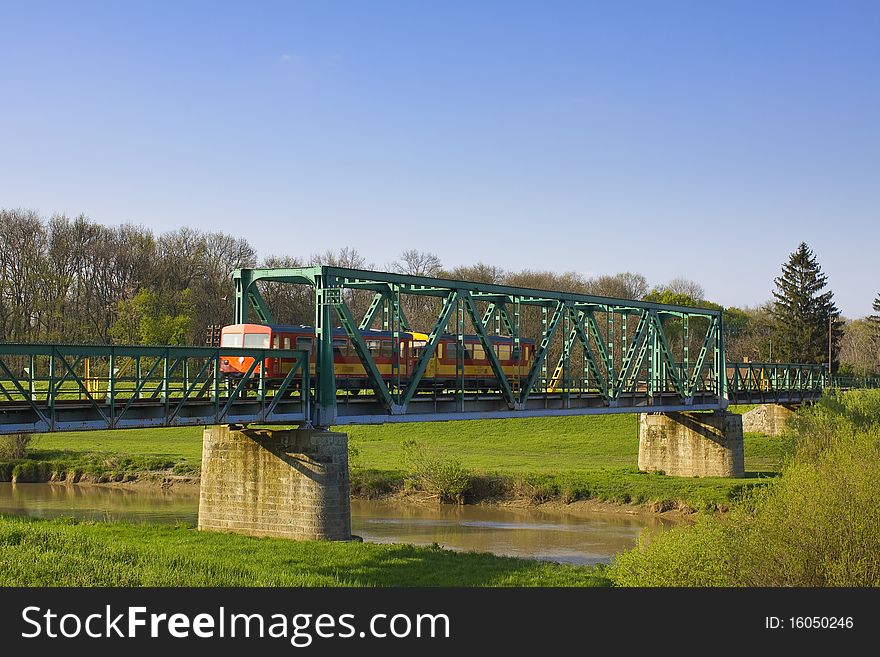 Small, red, urban train passing an old green iron bridge in europe. Small, red, urban train passing an old green iron bridge in europe