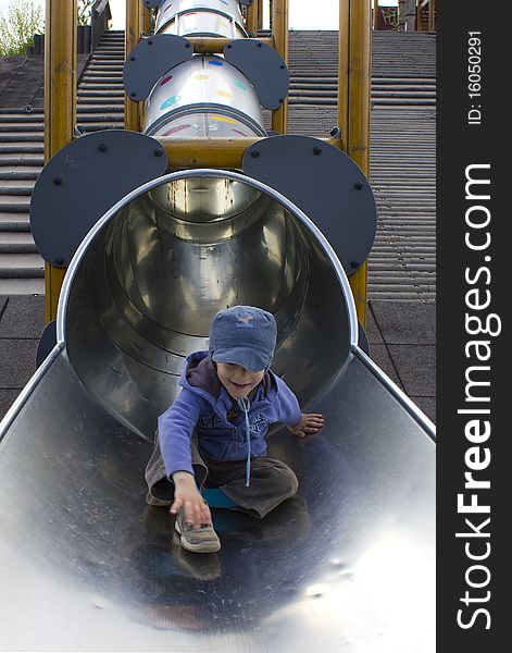 Young boy happily playing on a long slide. Young boy happily playing on a long slide