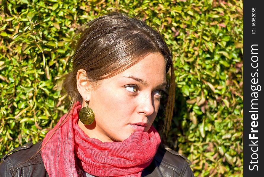 Beautiful girl in a red scarf. Against the backdrop of green hedges. Outdoor portrait.