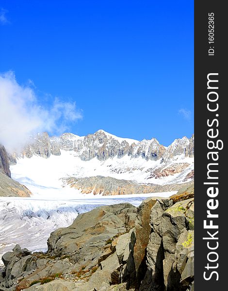 A snow capped mountain in Switzerland overlooking a glacier and a rocky hillside with clouds coming in. A snow capped mountain in Switzerland overlooking a glacier and a rocky hillside with clouds coming in