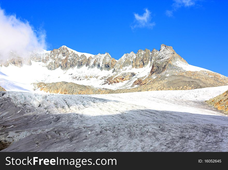 A snow capped mountain in  Switzerland and a rocky hillside with clouds coming in. A snow capped mountain in  Switzerland and a rocky hillside with clouds coming in