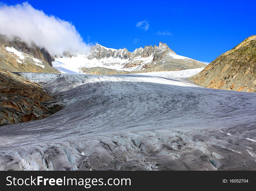 A snow capped mountain in Switzerland and a rocky hillside with clouds coming in over a glacier. A snow capped mountain in Switzerland and a rocky hillside with clouds coming in over a glacier