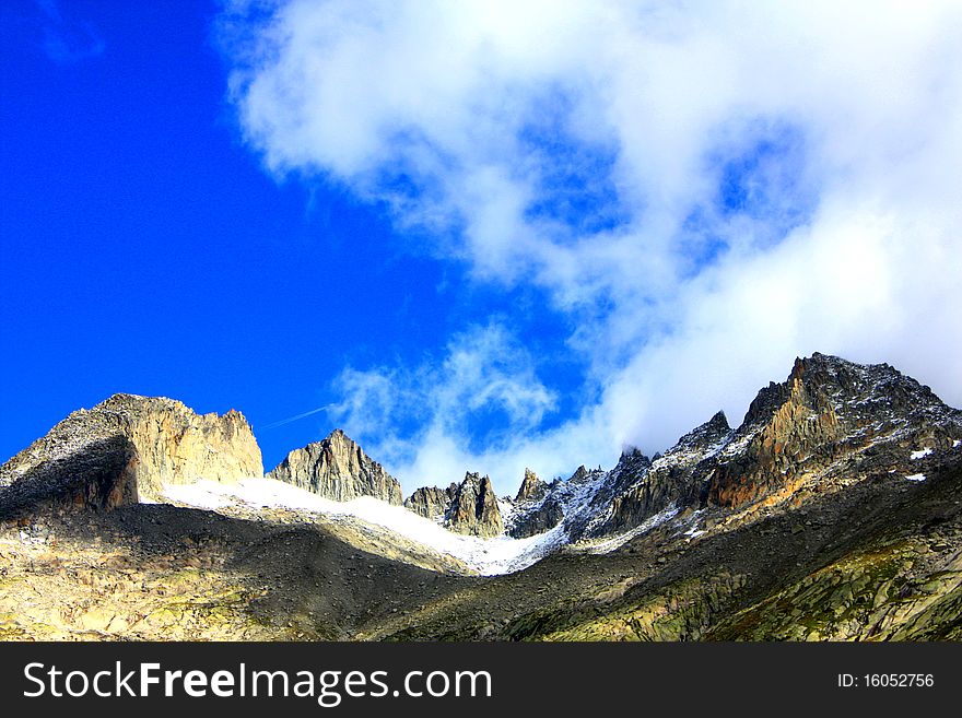 A snow capped mountain in Switzerland and a rocky hillside with clouds coming in. A snow capped mountain in Switzerland and a rocky hillside with clouds coming in