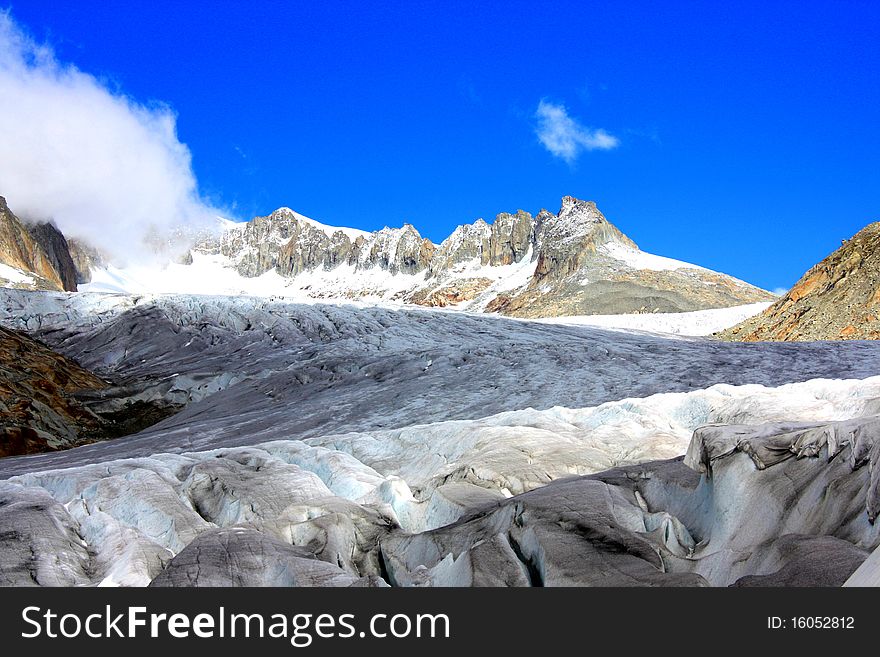 A snow capped mountain in  Switzerland overlooking a glacier and a rocky hillside with clouds coming in near passes in switzerland. A snow capped mountain in  Switzerland overlooking a glacier and a rocky hillside with clouds coming in near passes in switzerland