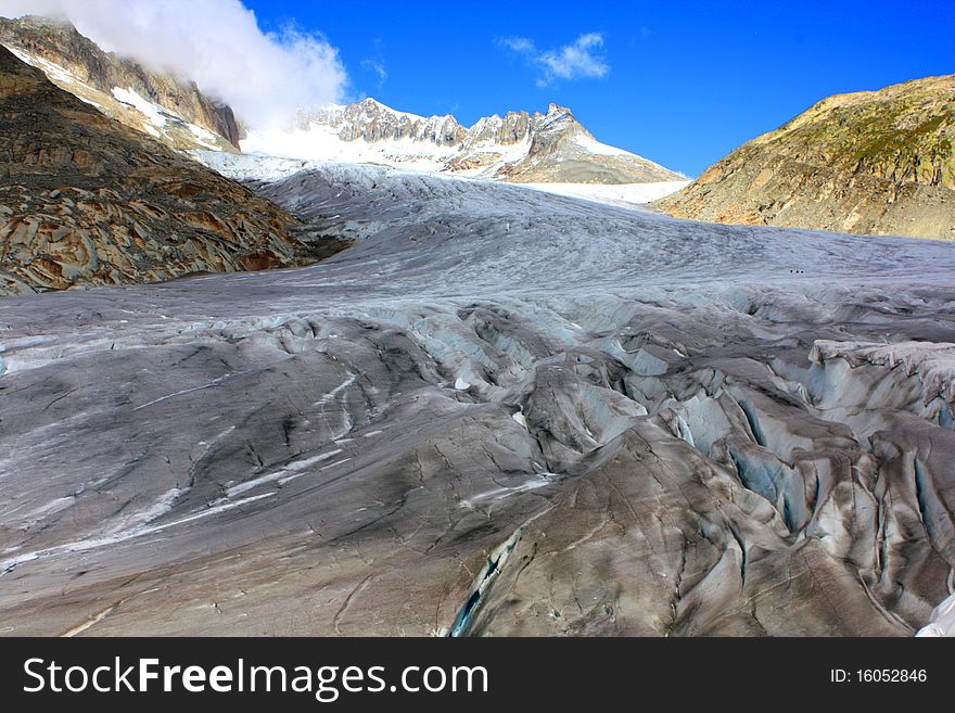A snow capped mountain in Switzerland overlooking a glacier and a rocky hillside with clouds coming in with a focus on the glacier. A snow capped mountain in Switzerland overlooking a glacier and a rocky hillside with clouds coming in with a focus on the glacier