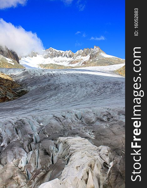 A snow capped mountain in Switzerland overlooking a glacier and a rocky hillside with clouds coming in with a focus on the glacier in a portrait photo. A snow capped mountain in Switzerland overlooking a glacier and a rocky hillside with clouds coming in with a focus on the glacier in a portrait photo