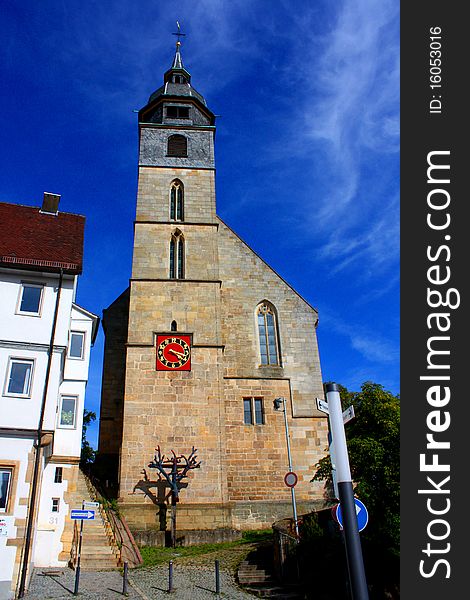 A old church in with a large steeple under a blue sky with a wooden cross and a red clock in Stuttgart in Germany. A old church in with a large steeple under a blue sky with a wooden cross and a red clock in Stuttgart in Germany