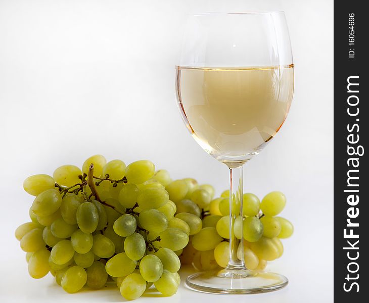 There are glass of white wine and grapes on a white background